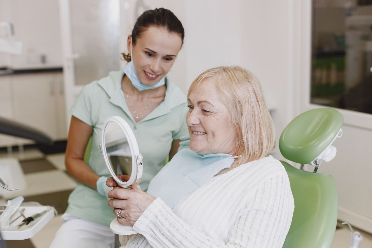 Senior patient smiling at her reflection with her dentist beside her