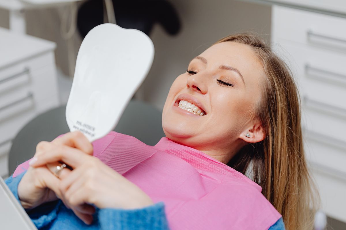 Smiling patient checking her teeth in a mirror at the dental clinic